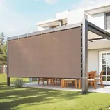 A modern outdoor pergola with a retractable privacy screen or shade, featuring a metal frame and wooden dining set underneath, situated by a contemporary house.