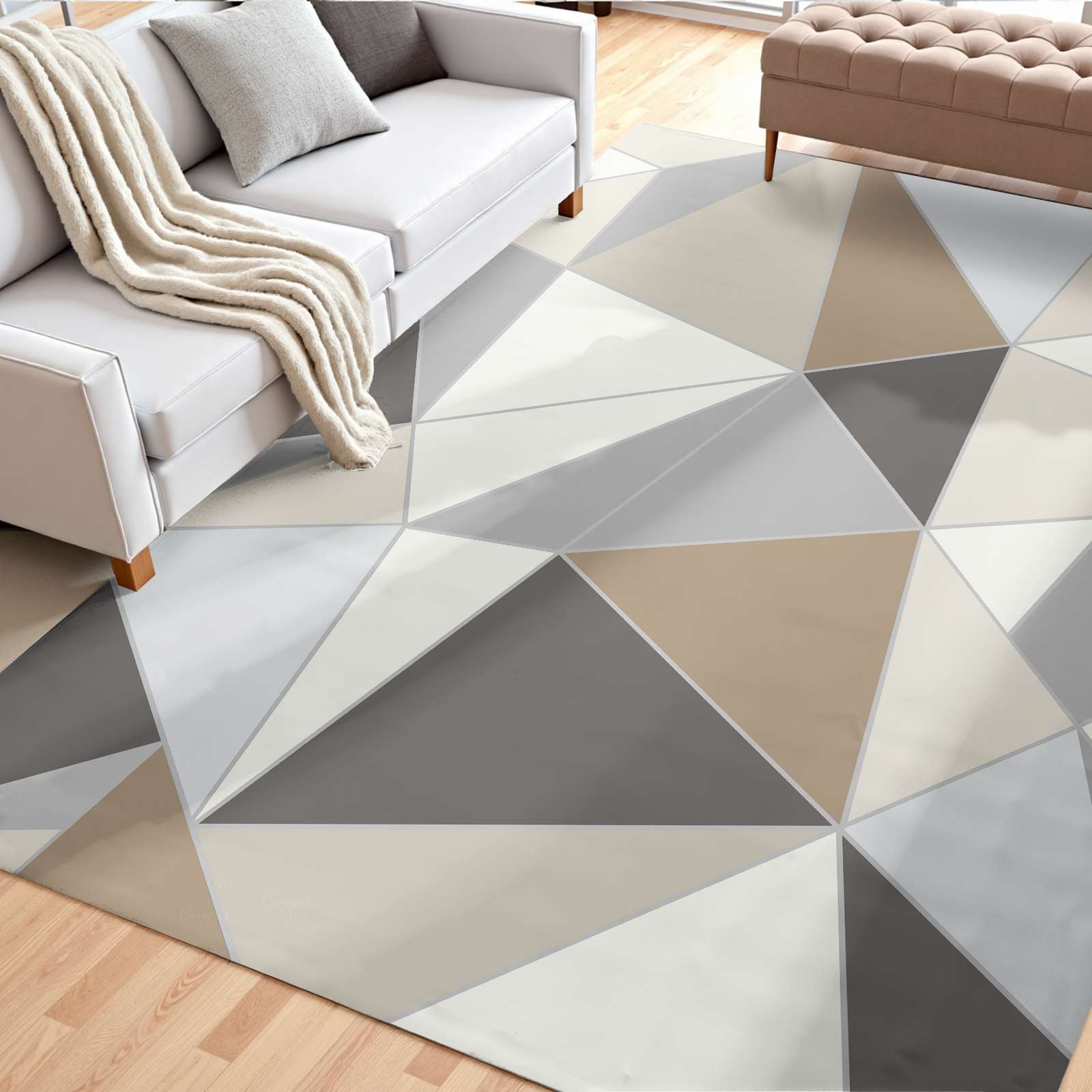 Modern geometric area rug with beige, gray, and white triangle pattern, placed in a living room with a white sofa, gray pillow, and cream blanket, on a light wood floor.