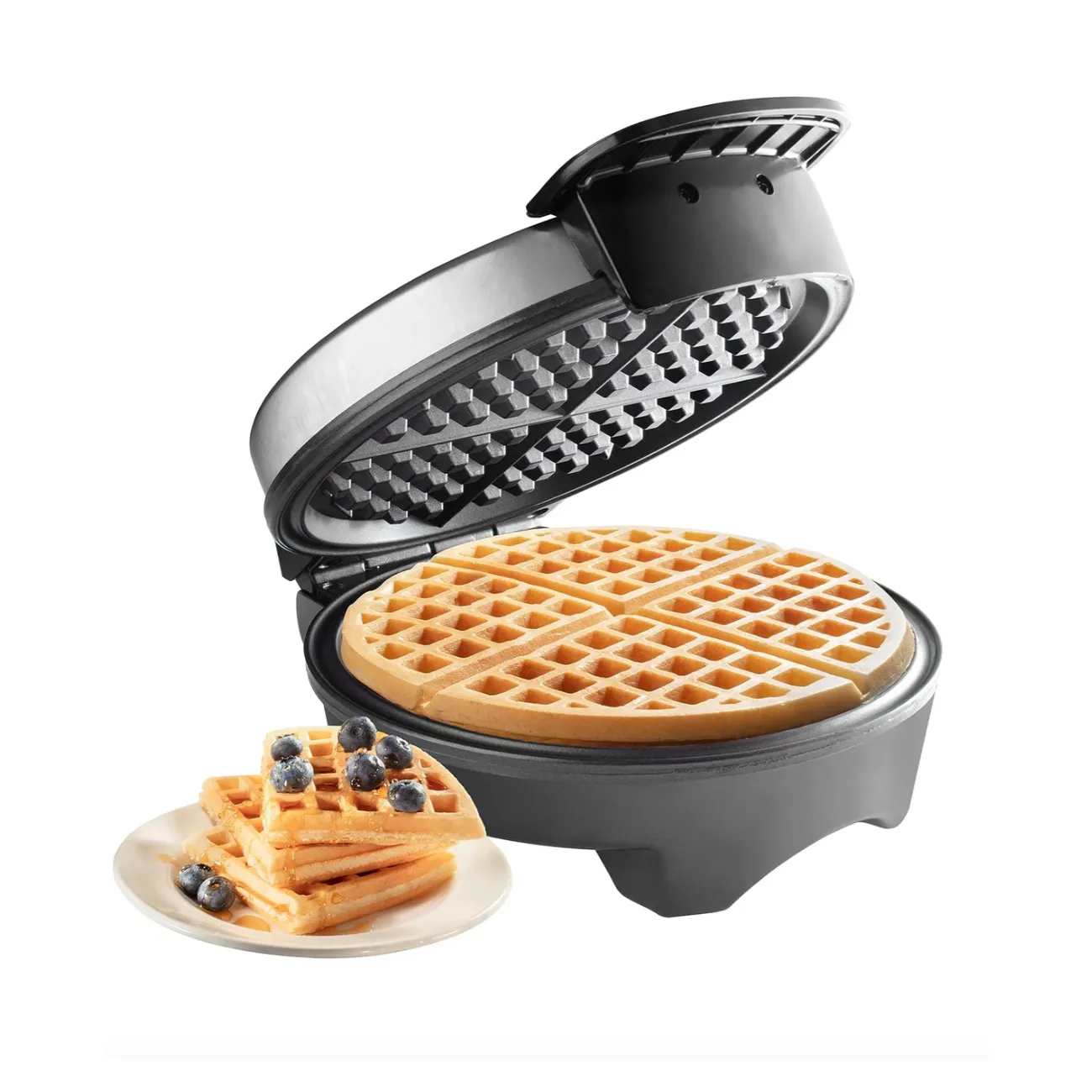 A waffle maker is open, displaying its checkered cooking plates, with a cooked round waffle on a plate beside it, garnished with blueberries.