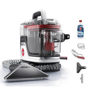 Compact portable carpet and upholstery cleaner with a transparent design, flexible hose, triangular head, and various cleaning attachments, accompanied by a bottle of Oxy stain remover.