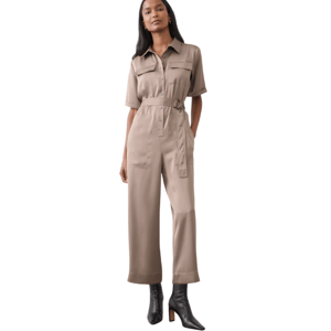 A woman is wearing a beige utility jumpsuit with short sleeves, button front, flap pockets, and a belted waist, paired with black pointed-toe ankle boots.