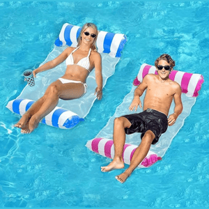 Two people are relaxing on inflatable pool loungers, each with striped blue-and-white and pink-and-white designs, floating in a clear blue pool.