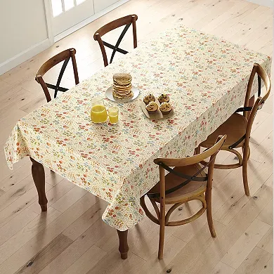 A rectangular tablecloth with a floral pattern in autumn colors covers a dining table, accompanied by a set of breakfast dishes.