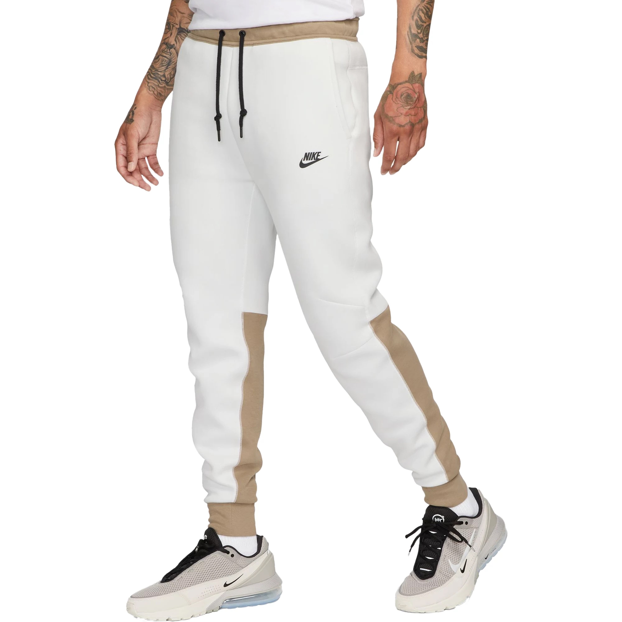 White and beige Nike Tech joggers feature a tapered design with a drawstring waist, side pockets, and a small black Nike logo on the left thigh.