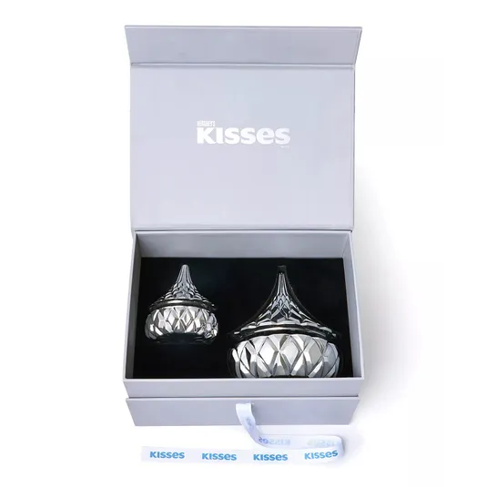 A gift box contains two crystal containers shaped like Hershey's Kisses, with intricate cut glass patterns and a blue \“Kisses\“ ribbon inside.