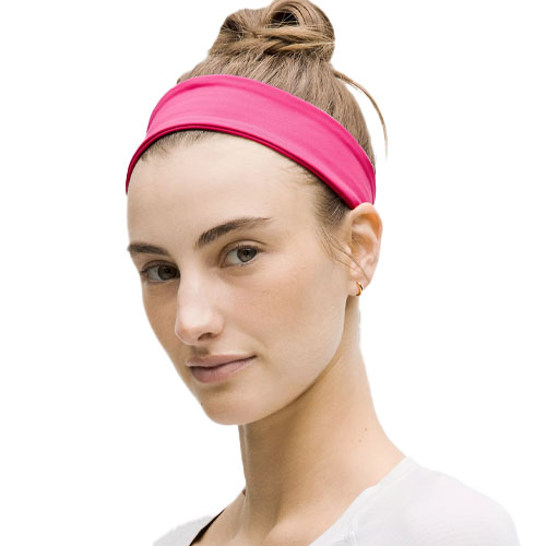 A person wearing a bright pink headband with hair styled in a bun, accompanied by a simple earring and a white shirt.