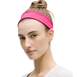 A person wearing a bright pink headband with hair styled in a bun, accompanied by a simple earring and a white shirt.