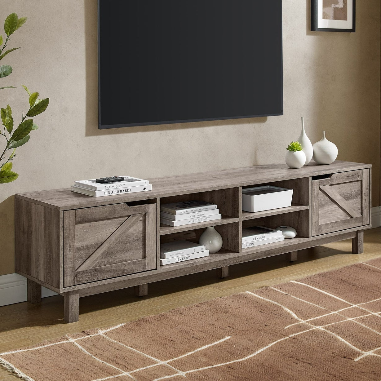 A 70\“ rustic TV stand with a wooden finish, featuring two sliding barn doors and open shelving for storage. It includes decorative items like vases and books, set against a light background with a modern aesthetic.