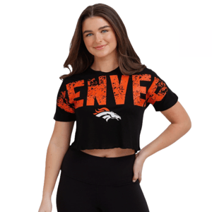 A woman is wearing a black crop top with \“Denver\“ in large distressed orange letters and a Denver Broncos logo. She is also wearing black leggings.
