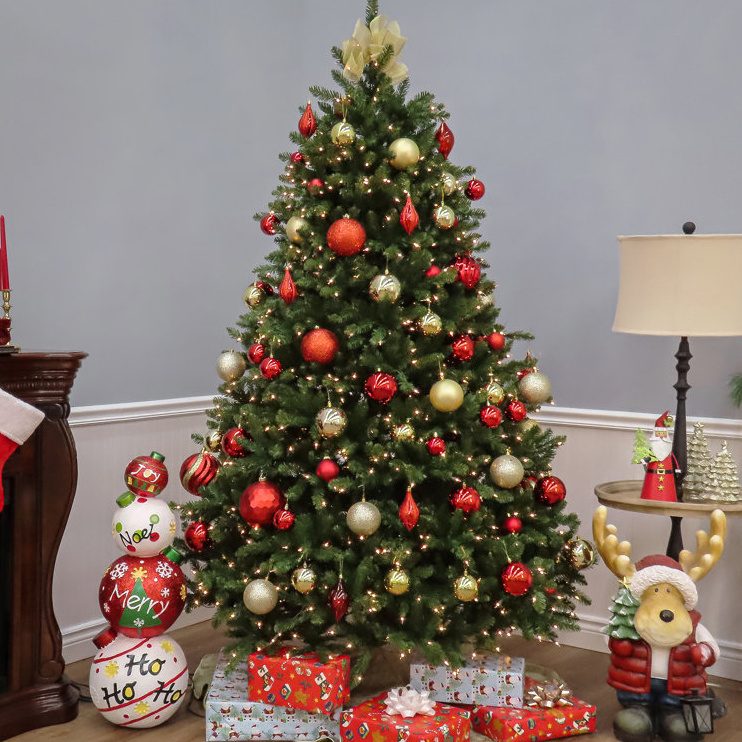7.5' Fir Christmas Tree with clear lights, adorned with red and gold ornaments. Presents wrapped in festive paper sit beneath, alongside a holiday-themed sculpture and decorative candles on a nearby table.