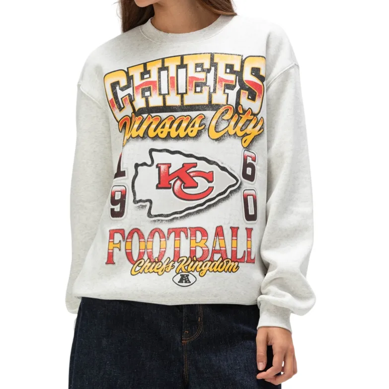 A woman is wearing a Kansas City Chiefs sweatshirt featuring the team's logo, \“Chiefs Kingdom,\“ and the year 1960, in red, yellow, and black text.