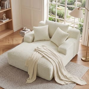 A cozy beige corduroy loveseat features plush cushions and a draped blanket, set in a bright room with wooden floors and a large window overlooking a garden.