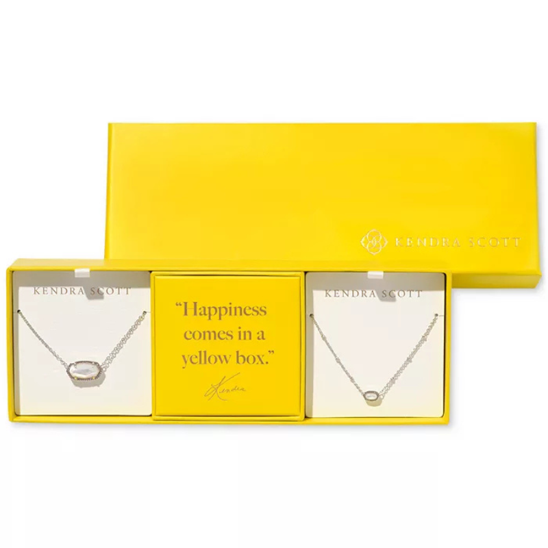 A yellow Kendra Scott box contains two necklace sets with oval pendants, separated by a card that reads, \“Happiness comes in a yellow box.\“
