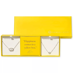 A yellow Kendra Scott box contains two necklace sets with oval pendants, separated by a card that reads, \“Happiness comes in a yellow box.\“