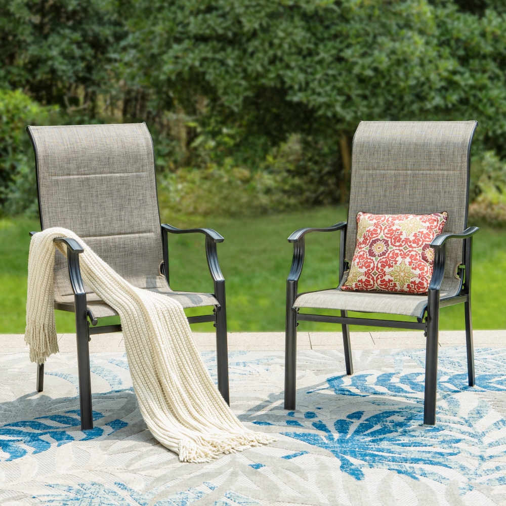 Two patio chairs with padded, grayish fabric seats and black metal frames. One chair has a white knit throw, and the other features a red and white floral cushion, placed on a blue and white patterned outdoor rug.