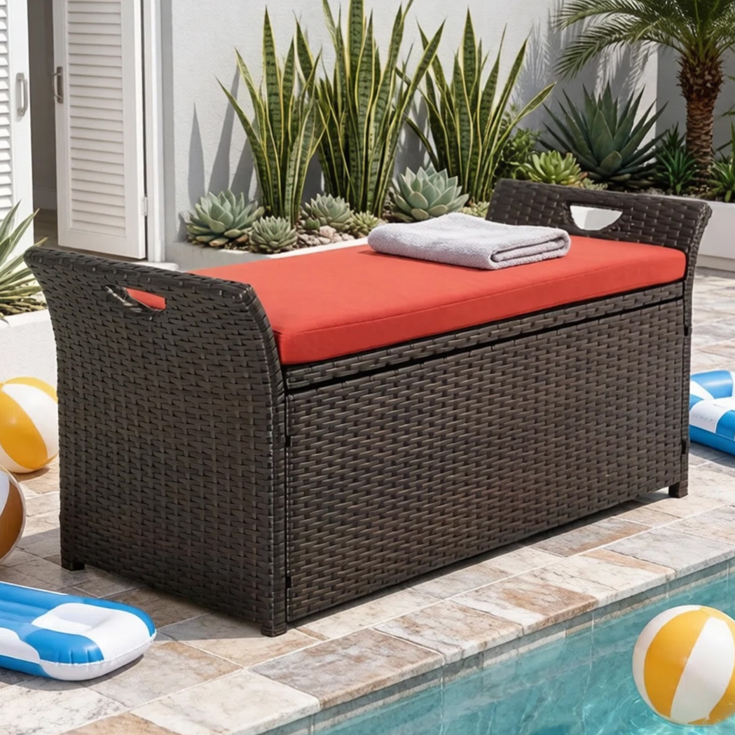 A wicker storage bench with a red cushion, located by a pool, surrounded by towels, a beach ball, and inflatables.
