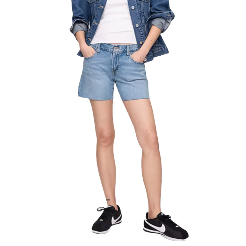 Mid-rise soft denim shorts, light blue, with a relaxed fit and casual style, feature a button and zip fly closure, pockets, and a slightly frayed hem. Paired with a denim jacket, white top, and black sneakers.