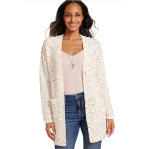 Woman wearing a speckled textured cardigan over a light pink top and blue jeans, accessorized with a pendant necklace.