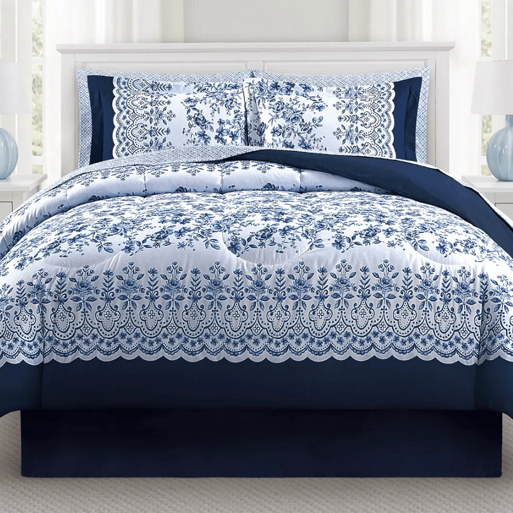 A navy and white bedding set featuring floral and lace patterns on the comforter and pillow shams, with a dark blue bed skirt.