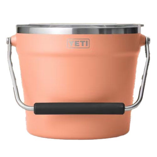 A peach-colored YETI bucket with a stainless steel rim and a black handle on a metal grip.