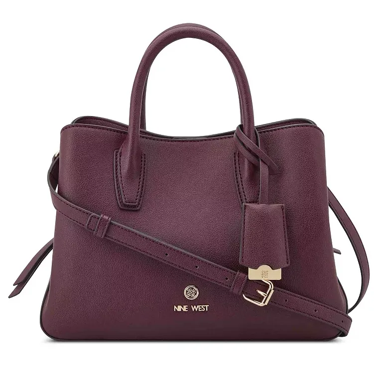 A purple Nine West handbag with top handles, a detachable shoulder strap, and a gold-tone logo accent, featuring a structured design and a luggage tag detail.