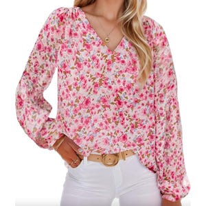 Women's floral blouse with a pink and white floral pattern, V-neck, and long sleeves. Paired with a tan belt and white pants, featuring a flowy, relaxed fit.