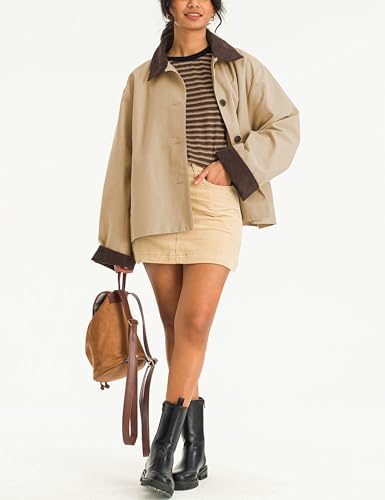 A person is wearing a beige jacket with a dark collar, striped shirt, and beige skirt, paired with black boots. They are holding a brown backpack.