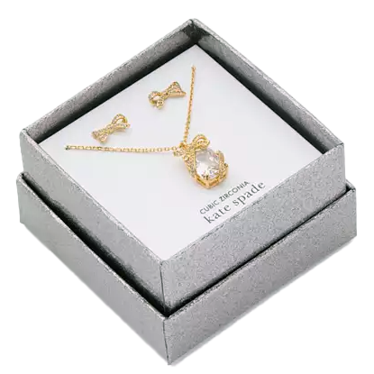 A jewelry set featuring a gold-colored necklace with a large, clear cubic zirconia stone and matching bow-shaped earrings is displayed in a silver gift box.