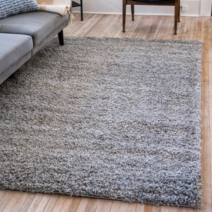 A 5' x 8' gray shag rug with a thick, plush texture is placed on a light wooden floor beside a gray sofa and a wooden chair.