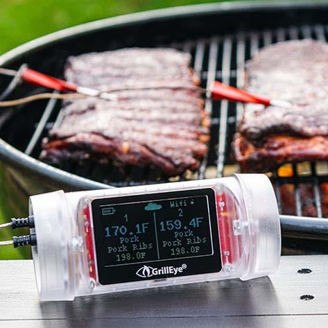 A barbecue grill with ribs cooking on it and a digital meat thermometer displaying temperatures.
