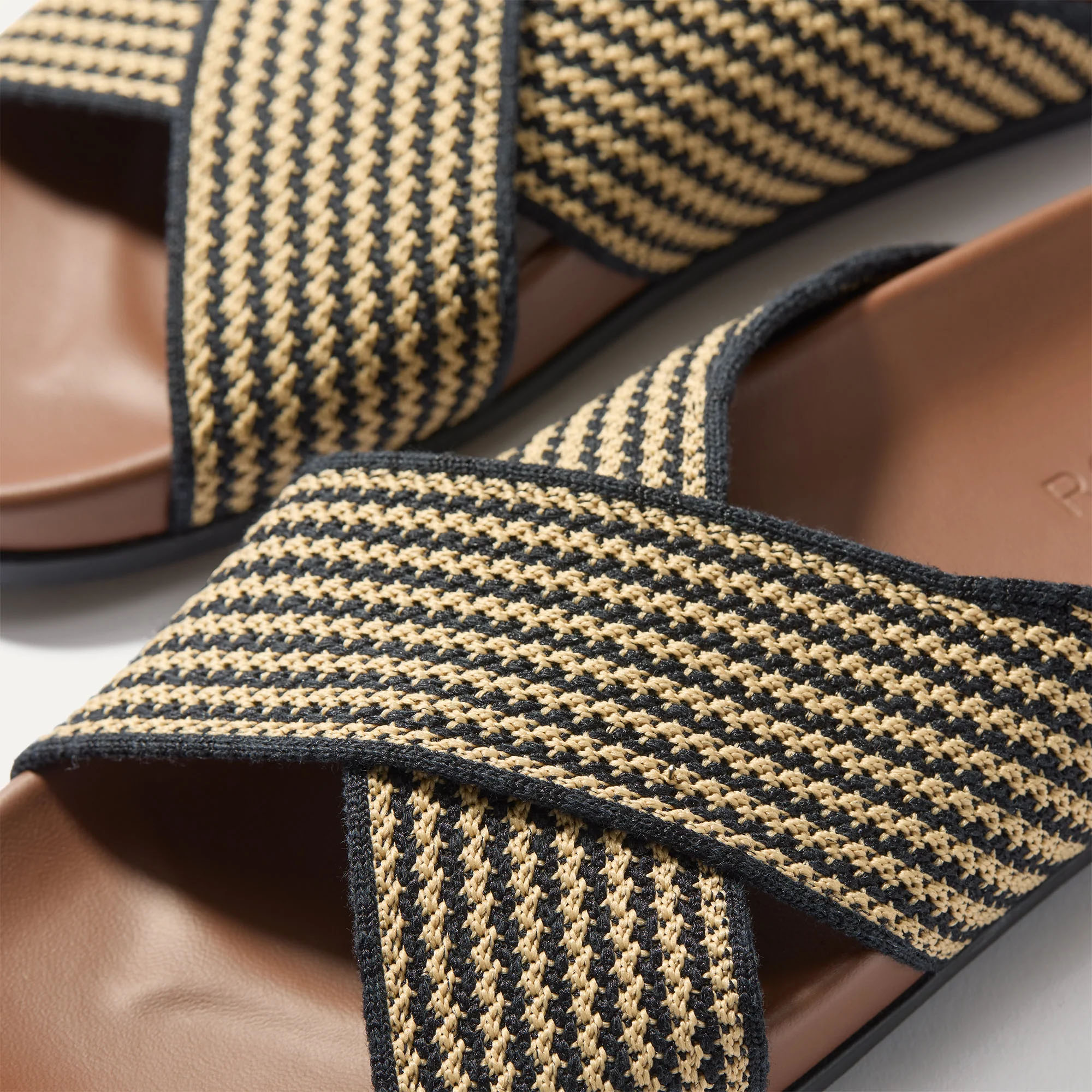 Rothy's Weekender Sandals feature crisscross straps with a black and beige woven pattern on a brown footbed. The design is casual and suitable for relaxed outings.