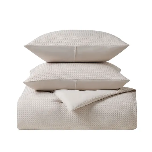 A beige textured bedding set featuring two stacked pillows on top of a folded duvet or blanket.