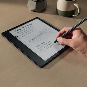 A person is writing on a digital tablet with a stylus pen, with a mug beside the tablet.