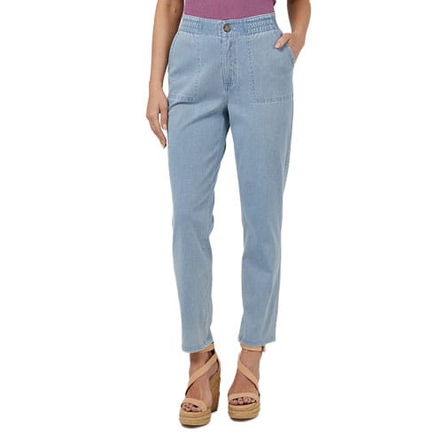 Light blue jeans with an elastic waistband, front pockets, and a button closure are worn by a person paired with tan wedge sandals and a purple top.