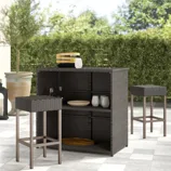 Outdoor bar set with a wicker design includes two bar stools and a bar counter with shelves, featuring decorative bowls and glasses.
