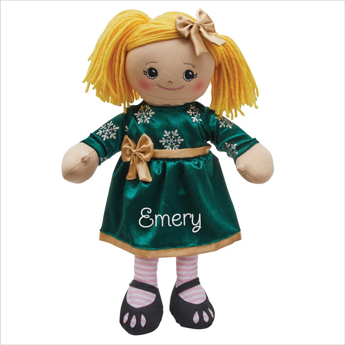 A plush doll with yellow yarn hair, wearing a green dress adorned with snowflakes and a gold bow, personalized with the name \“Emery.\“ The doll has striped pink socks and black shoes.
