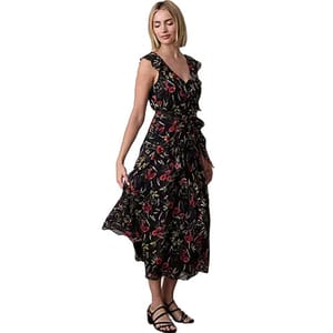 A woman is wearing a sleeveless, black floral maxi dress with red and green patterns, paired with black sandals.