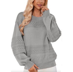 A gray knit sweater features intricate lace patterns on the yoke and sleeves, with a relaxed fit and ribbed cuffs and hem.