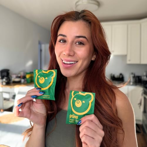 A woman is holding two packets of \“grüns\“ gummies, each with packaging featuring a yellow bear design on a green background.