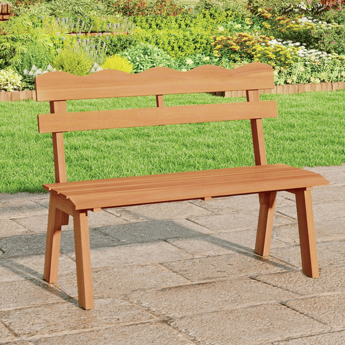 A wooden garden bench with a scalloped backrest is placed on a stone patio, surrounded by lush greenery and vibrant flowers.