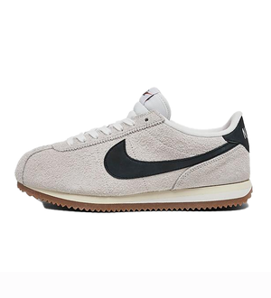 Nike Cortez Vintage Suede Shoes feature a light gray suede upper with a classic black Nike Swoosh, white laces, and a gum sole. The style is retro and casual.