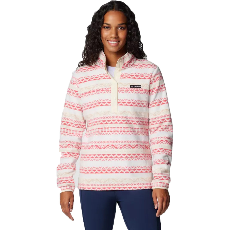 A woman is wearing a Columbia printed fleece with a red and white geometric pattern and a half-zip front. The fleece features a Columbia logo on the chest.