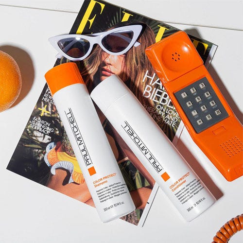 a white shampoo and conditioner besides an orange and an orange phone