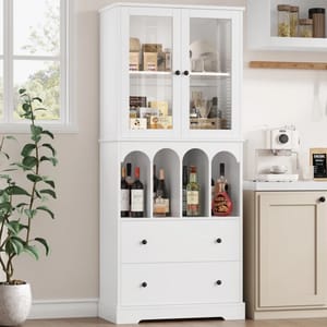 A white 71\“ kitchen pantry with a top section of glass doors displaying food items, a middle section with arches storing various bottles, and two bottom drawers. It's next to a coffee machine and accompanied by a potted plant.