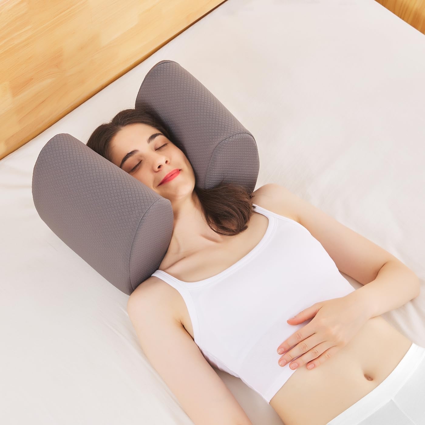 A woman lying on a bed with a unique gray neck support pillow cradling her head and neck.