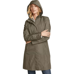 A woman is wearing a khaki hooded raincoat over a white shirt and blue jeans.