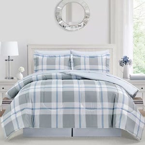 A bedroom set featuring a plaid-patterned comforter and two matching pillow shams in shades of gray and white, with a simple decor including a round wall mirror, table lamp, and vase with flowers.