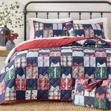 A quilt set featuring a patchwork design with ribbon-like patterns in blue, red, green, and white, accompanied by matching pillow shams. A matching carrying case is included.