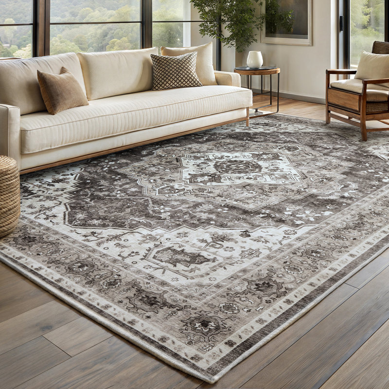 A large boho-patterned rug, measuring 8'x10', features intricate geometric and floral designs in shades of brown and cream. It's placed in a modern living room with a cream sofa and wooden armchair.