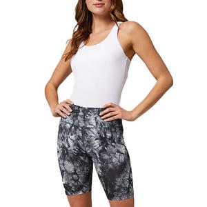A woman is wearing a white sleeveless top paired with black and gray tie-dye print cycling shorts.